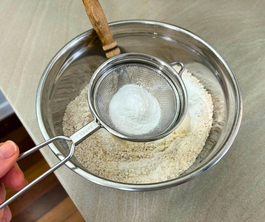 Baking powder being sifted into freshly milled organic purple straw wheat being used to prepare homemade wholegrain scones.